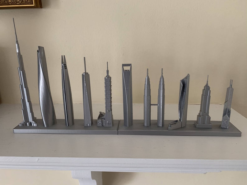 May include: A collection of silver-colored miniature skyscraper models displayed on a shelf. The models vary in design and height, showcasing architectural diversity. The display includes iconic buildings from around the world.
