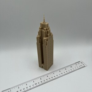 May include: A beige 3D printed model of a skyscraper with a pointed roof and a ruler for scale.