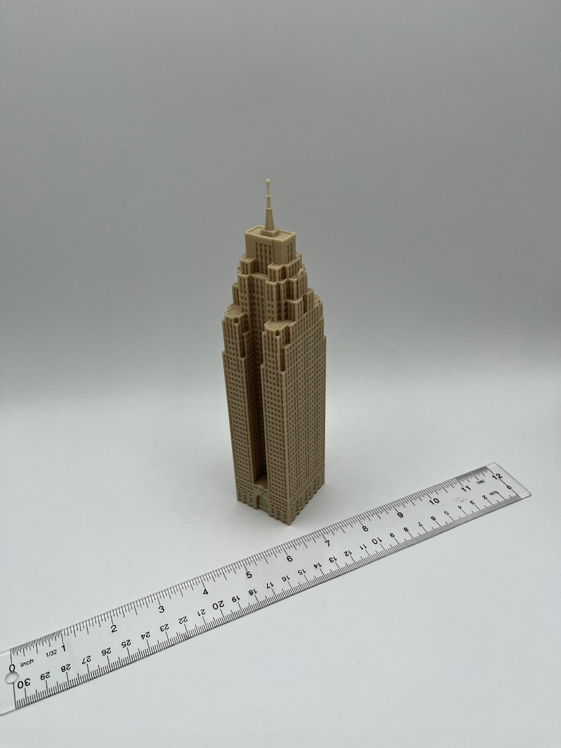 May include: A beige 3D printed model of a skyscraper with a pointed roof and a ruler for scale.