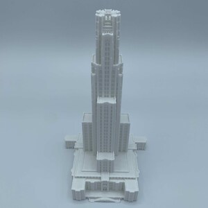 May include: A white 3D printed model of a tall building with a pointed roof and many windows.