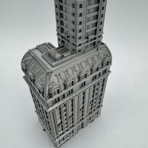 May include: A detailed 3D printed model of a tall, gray building with intricate architectural details. The building has a rectangular base and a tall, narrow tower.