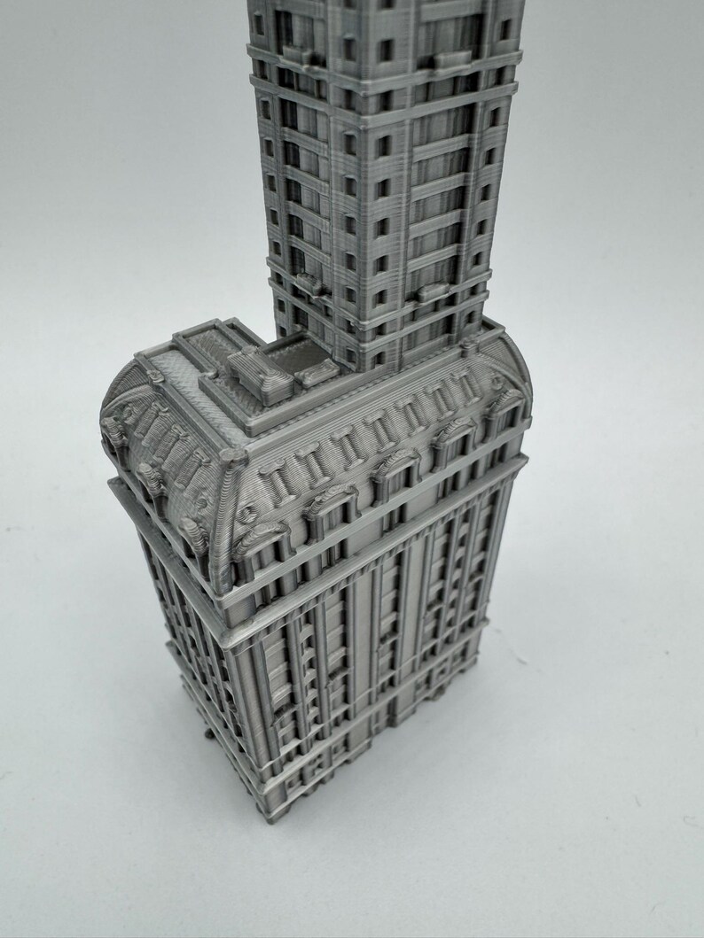 May include: A detailed 3D printed model of a tall, gray building with intricate architectural details. The building has a rectangular base and a tall, narrow tower.
