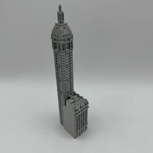 May include: A gray 3D printed model of a tall building with a domed roof.