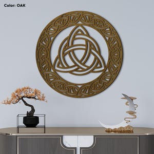 May include: Oak-colored wooden wall art featuring a Celtic knot design within a circular frame. The artwork is displayed on a white wall, with the text "Color: OAK" in the upper left corner. The piece is part of a home decor collection.