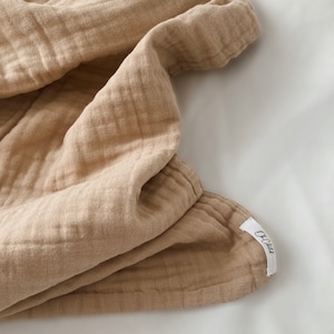 May include: A light brown muslin blanket with a white tag that says "OC Child" on it.