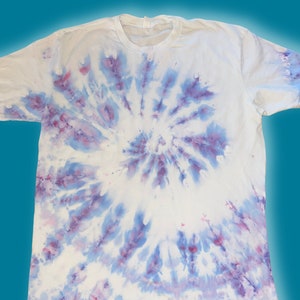 Op de afbeelding: Een wit T-shirt met een blauw en paars tie-dye patroon. Het patroon is een spiraalvormig ontwerp met een wit centrum.