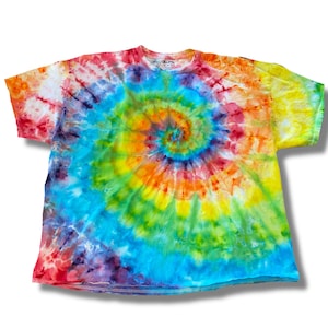 Op de afbeelding: Een tie-dye T-shirt met een regenboogspiraalpatroon. Het shirt is wit met tinten rood, oranje, geel, groen, blauw en paars.