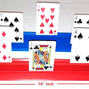May include: A red and blue card holder with 10 playing cards arranged in a row. The cards are a mix of suits and numbers, including 10 of clubs, 7 of diamonds, Jack of clubs, 4 of spades, 2 of clubs, and 5 of hearts. The holder is 10 inches long.