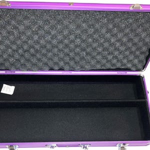 May include: Open purple aluminum case with a black interior. The top half of the case is lined with black foam. The bottom half has a black felt lining with a divider. The case has silver latches and hinges.
