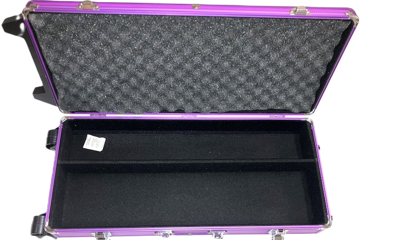 May include: Open purple aluminum case with a black interior. The top half of the case is lined with black foam. The bottom half has a black felt lining with a divider. The case has silver latches and hinges.