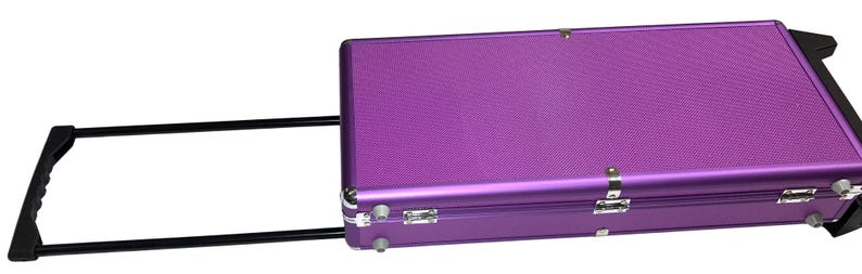 May include: A purple rolling suitcase with a textured surface. The suitcase has a black handle and black wheels. The case is rectangular and has silver latches and hinges.