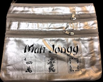 May include: Silver Mah Jongg bag with three zippered compartments. The bag features the text "Mah Jongg" in a stylized font, along with three illustrated tiles. The bag is made of a shiny, metallic material.