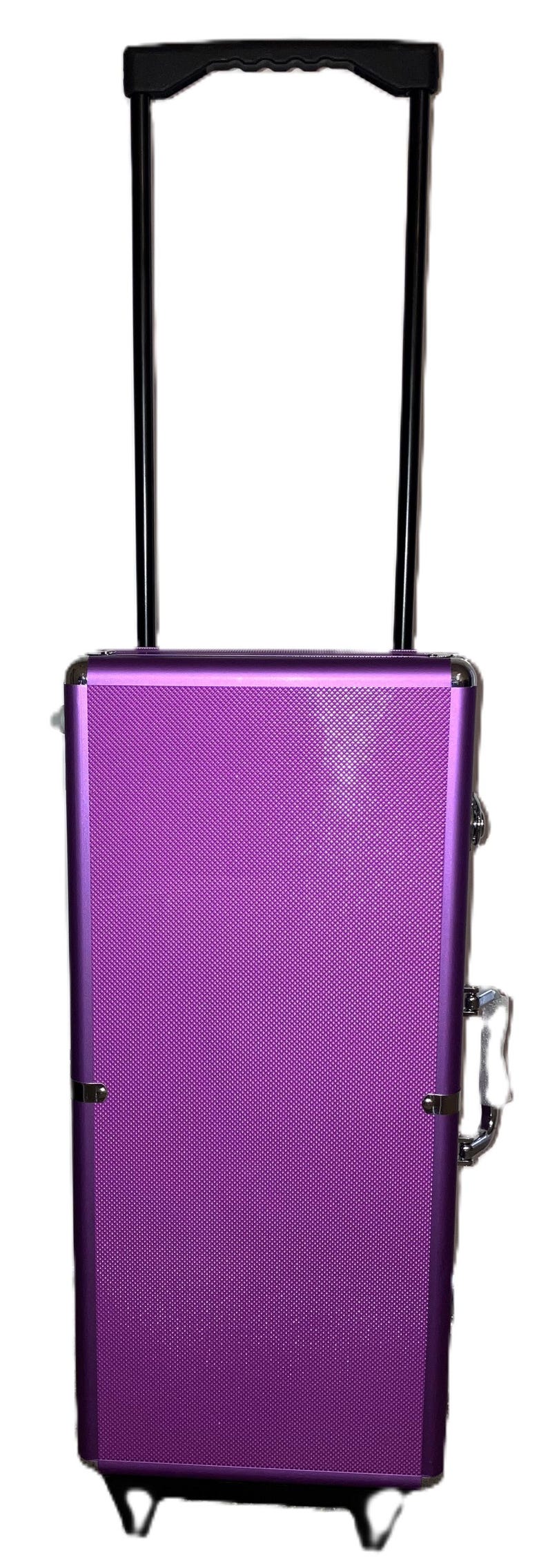 May include: A purple rolling makeup case with a textured surface. It has a black telescoping handle and silver-colored hardware. The case is designed for cosmetics and beauty supplies.
