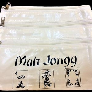 May include: Off-white Mah Jongg bag with three zippered compartments. The bag features the words "Mah Jongg" in black script, along with three illustrated game tiles. The bag is rectangular and has a glossy finish.