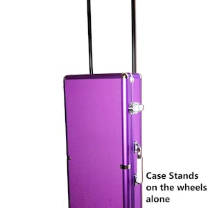 May include: A purple rolling case with a black handle and wheels. The case has silver-colored metal accents and latches. The text "Case Stands on the wheels alone" is visible on the side of the case.