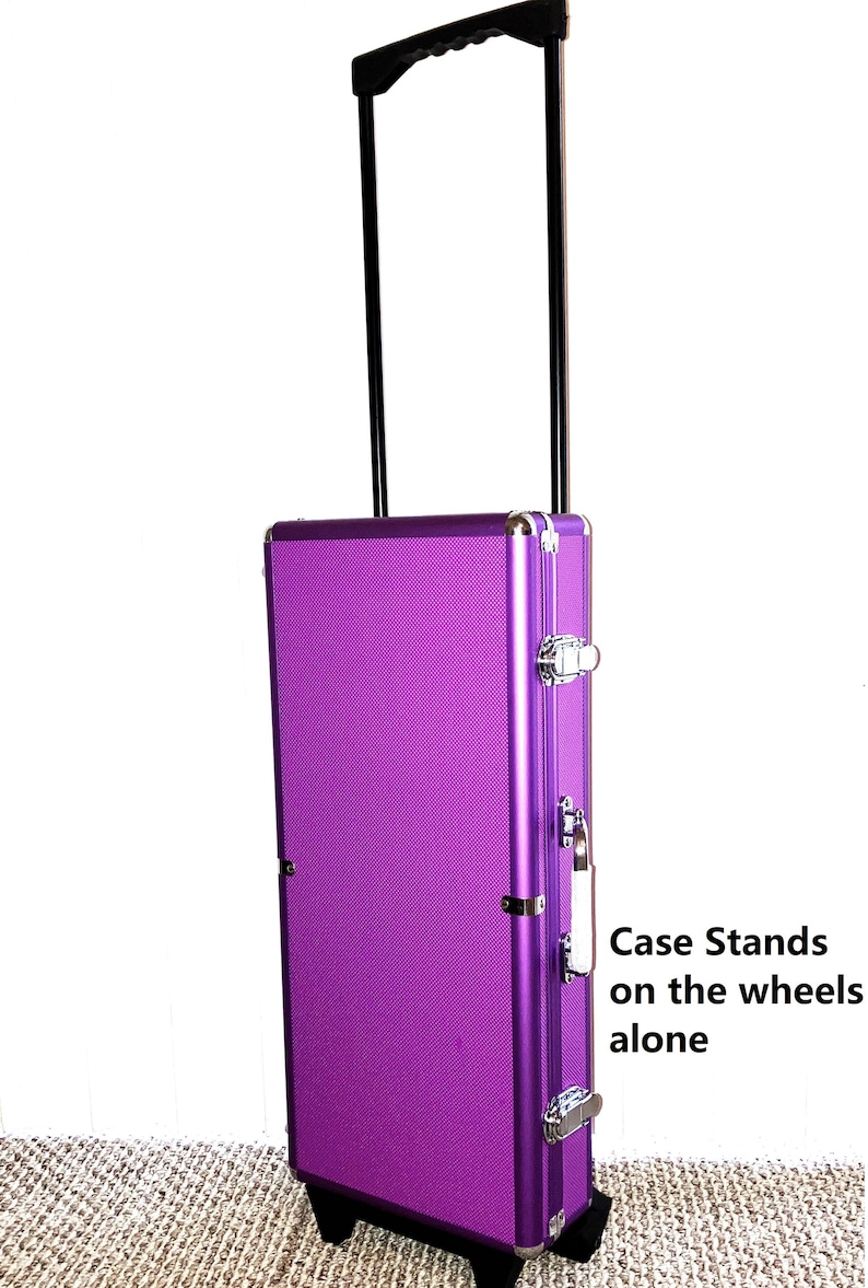 May include: A purple rolling case with a black handle and wheels. The case has silver-colored metal accents and latches. The text "Case Stands on the wheels alone" is visible on the side of the case.