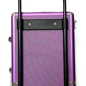 May include: A purple rolling makeup case with a textured surface and black handle. The case has a telescoping handle and wheels for easy transport. The case is designed for cosmetics and beauty supplies.