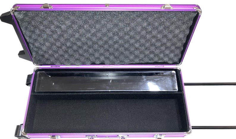 May include: Open purple aluminum case with a black interior. The top of the case has a foam lining. The bottom of the case has a black felt lining. A clear plastic tray is in the middle of the case.