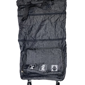 May include: A dark gray, foldable shopping cart with a black handle and wheels. The cart has a large front pocket with three white decorative designs. The cart is made of a textured fabric and is designed for easy storage and transport.