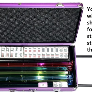 May include: A purple wheeled case, open to reveal a black foam interior and various Mahjong tiles and racks. The case has a handle and is designed to hold 166 tiles and 4 racks. Text on the image states the case is empty.