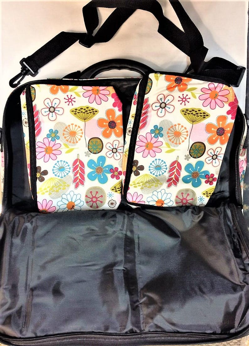 Op de afbeelding: Open zwarte reistas met twee bloemenprint compartimenten. De compartimenten hebben een cr&egrave;mekleurige achtergrond met kleurrijke bloemen in roze, oranje, blauw en geel. Een zwarte schouderriem en handvat zijn zichtbaar.