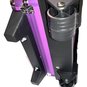 May include: A purple rolling makeup case with black corner supports and wheels. The case has a silver metal clasp and a textured purple center panel. The wheels are black and the case is designed for easy transport.