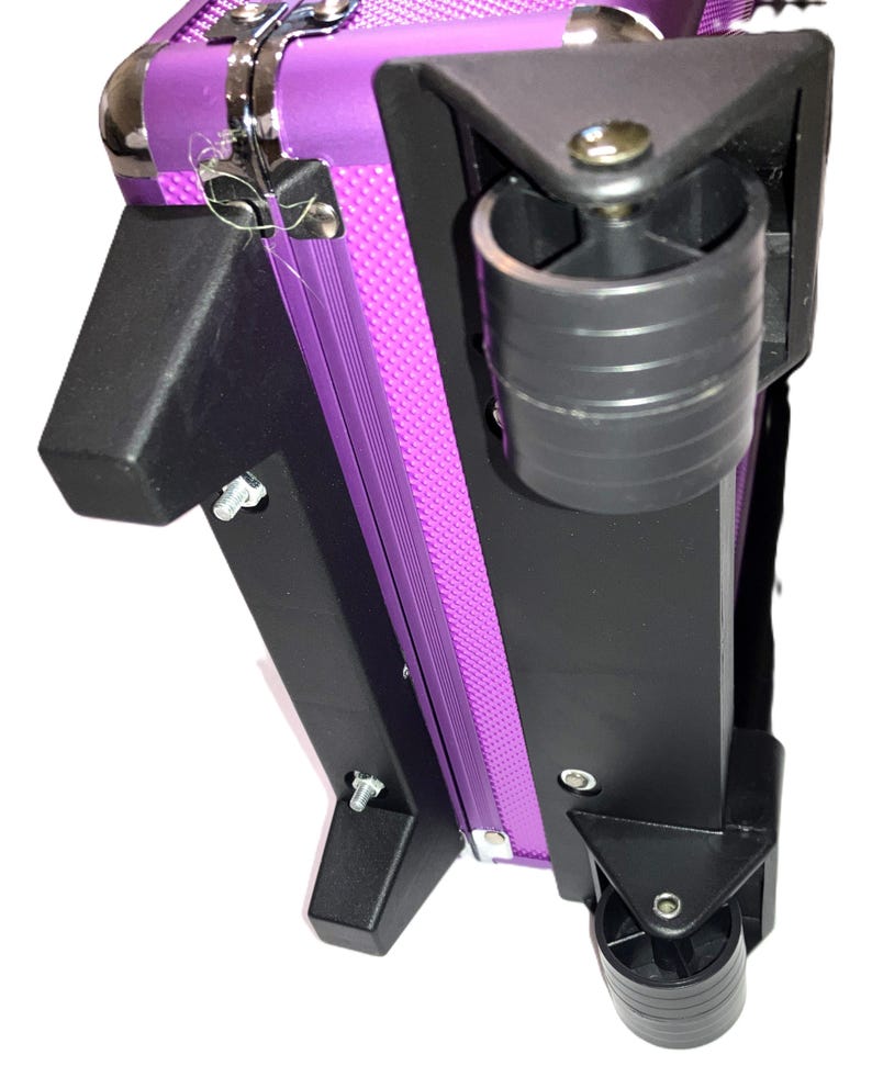 May include: A purple rolling makeup case with black corner supports and wheels. The case has a silver metal clasp and a textured purple center panel. The wheels are black and the case is designed for easy transport.