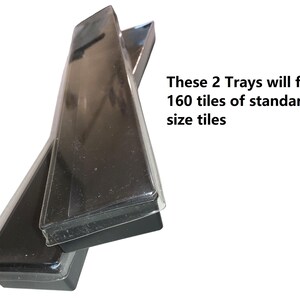 Op de afbeelding: Twee zwarte rechthoekige trays met doorzichtige plastic deksels zijn onder een hoek gestapeld. De tekst op de afbeelding geeft aan dat de twee trays 160 tegels van standaardformaat zullen bevatten. De trays lijken leeg te zijn.