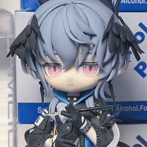 May include: A detailed figurine of an anime-style character with pale blue hair and red eyes. The figure wears a black and blue outfit with intricate details, including black wing-like accents and a long, flowing cape. The character holds a thin, silver object.