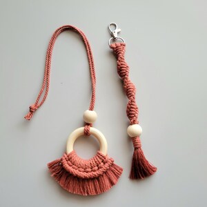 May include: A set of two macrame necklaces with wooden beads and tassels. The necklace on the left has a ring and a larger tassel. The necklace on the right has a smaller tassel and a silver clasp.