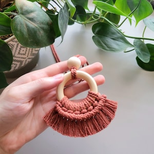 May include: A terracotta macrame necklace with a wooden ring and bead. The necklace has a fringe detail.
