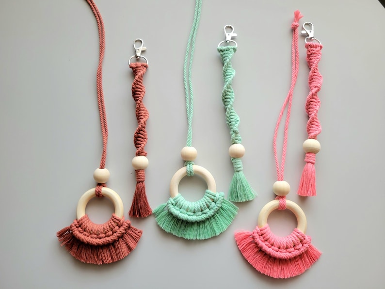 May include: Four macrame keychains with wooden rings and tassels. The keychains are in shades of pink, red, and green.