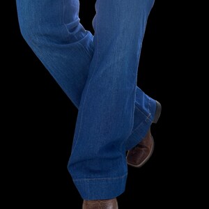 May include: Blue denim jeans with a flared leg design. The jeans are paired with brown leather square-toe boots. The image is set against a black background, highlighting the clothing and footwear.
