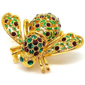 May include: A gold-tone bee brooch with red and green enamel and rhinestones. The bee has a round body and two wings.