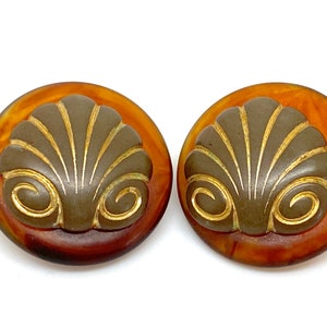 Può includere: Un paio di orecchini vintage a forma di conchiglia, di colore marrone e oro. Gli orecchini sono in plastica e hanno un effetto marmorizzato.