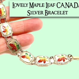 May include: Silver bracelet featuring rectangular links with colorful maple leaf designs. The bracelet has a gold clasp and is labeled "Lovely Maple Leaf Canada Silver Bracelet". The leaves are red, yellow, and green.