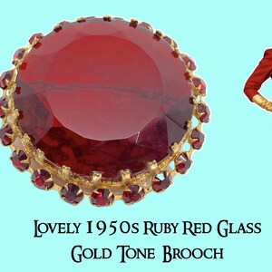 Op de afbeelding: Een ronde goudkleurige broche met een grote, gefacetteerde robijnrode glazen middensteen, omringd door een rand van kleinere, bijpassende rode glazen stenen. De tekst luidt: LOVELY 1950S RUBY RED GLASS GOLD TONE BROOCH. Een figuur in het rood is zichtbaar.