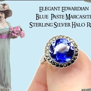 May include: An Elegant Edwardian sterling silver halo ring with a large blue paste center stone and marcasite accents. The ring is held up by a finger. The image also includes a vintage illustration of a woman in an Edwardian dress.