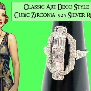 Pode incluir: Anel cl&aacute;ssico em estilo Art Deco com pedras de zirc&ocirc;nia c&uacute;bica em prata 925. O anel apresenta um design central retangular com pedras menores ao redor. &Eacute; exibido em um suporte preto sobre um fundo verde.