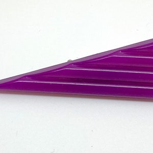 May include: A purple plastic hair clip shaped like a triangle with a ribbed design.