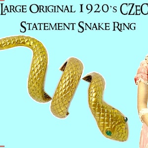 May include: A large, gold-coloured statement ring in the shape of a snake, with a textured scale pattern. The ring has a green gem for an eye. The text in the image reads "Large Original 1920's Czech Statement Snake Ring."