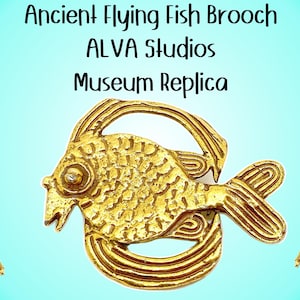 Puede incluir: Broche de metal dorado en forma de pez volador. La broche es una réplica de un artefacto antiguo. El texto "Ancient Flying Fish Brooch ALVA Studios Museum Replica" se muestra sobre la broche.