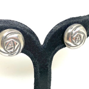May include: A pair of silver earrings with a rose design. The earrings are on a black velvet display stand.