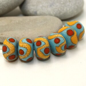 May include: A string of six round beads with a blue, yellow, and orange pattern. The beads are made of clay and have a textured surface.