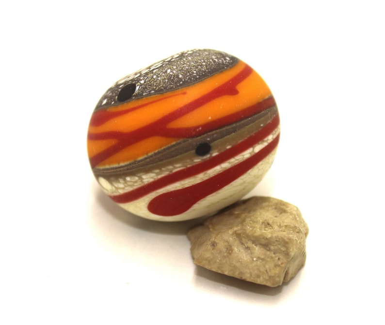 May include: A round, multi-coloured glass bead with orange, red, brown, and white stripes. The bead has a speckled, silver-like finish.