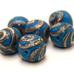 Può includere: Un set di sei perline di vetro rotonde di colore blu e bianco con un motivo a spirale. Le perline hanno un foro al centro per essere infilate.