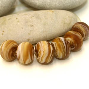 May include: A strand of brown and white swirl glass beads. The beads are round and have a marbled appearance.