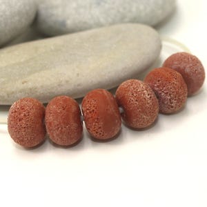 May include: A strand of six red lava rock beads with a rough, textured surface.