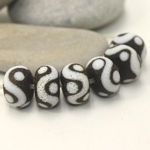 May include: A strand of six white and brown ceramic beads with a swirling pattern. The beads are round and have a smooth, glossy finish.