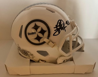 Könnte beinhalten: Ein weißer Football-Helm mit dem Logo der Pittsburgh Steelers, einem schwarz-goldenen Emblem und dem Wort "Steelers". Der Helm hat eine Unterschrift und die Nummer 43. Der Helm steht auf einer weißen Box.